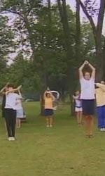 6 people standing on grass, trees behind them.  The people are stretching, with arms in the air.