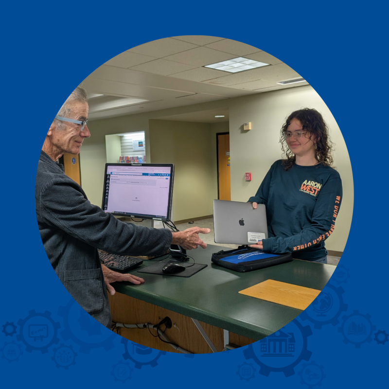 A woman is on one side of a counter, holding a laptop. A man stands on the other side of the counter and is reaching for the laptop.