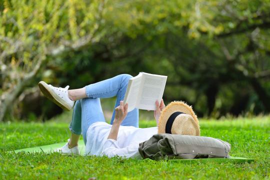Woman reading a book, while lying on grass.