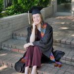 Woman sitting on brick steps.  She is wearing a graduate gown.
