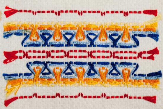 Example of Swedish weaving, beige background with horizontal lines of red, orange flames and blue water. 