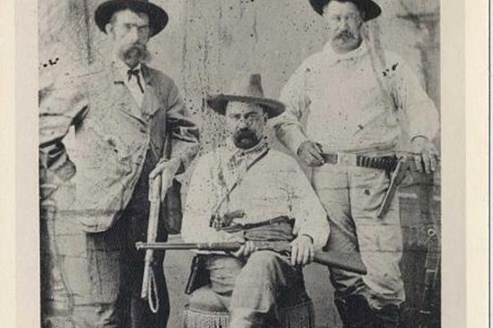 3 men face the camera. All three are wearing cowboy hats and western garb.