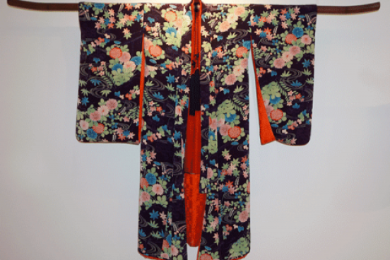 Kimono displayed on a wall.  Black background with flowers of green, pink and blue.  The inside of the kimono is red.