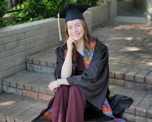 Woman sitting on brick steps.  She is wearing a graduate gown.