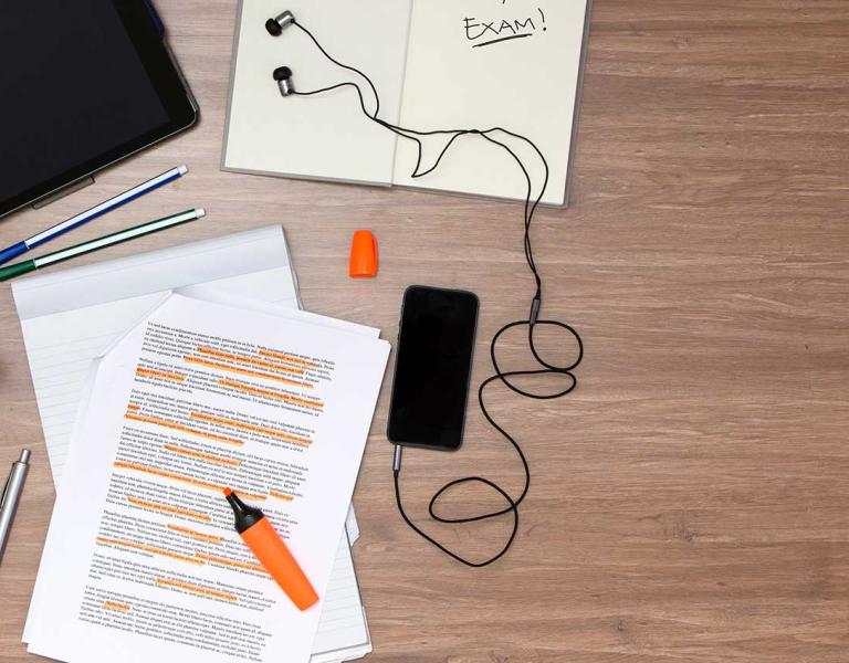 Pen, paper, phone, earbuds, tablet all on a table.