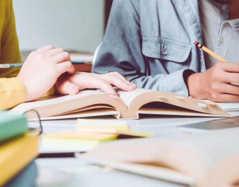 Two people looking over a book, pencils in hands.