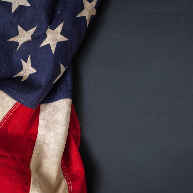 Dark blue background, on the left side is a flag, the stars and stripes are visable.