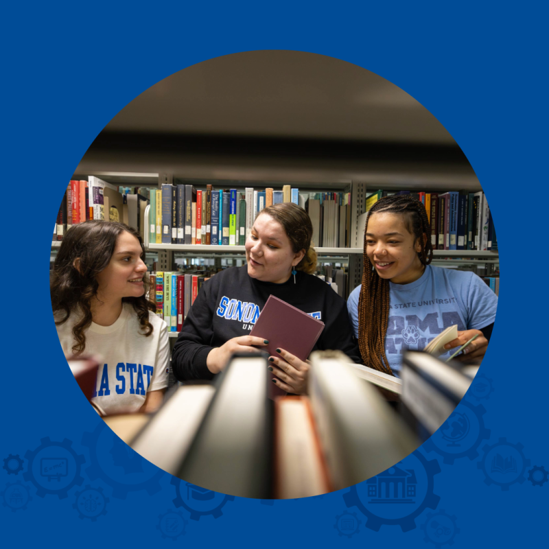 3 people standing in front of bookshelves,  looking at books.