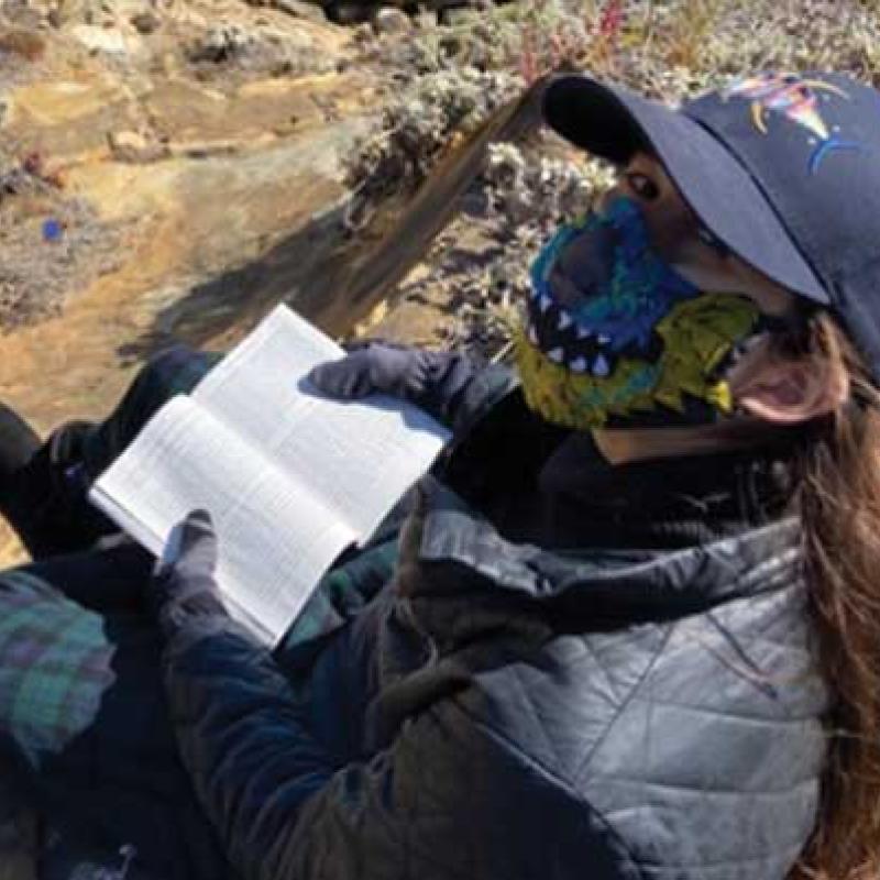 Woman wearing a mask, reading a book.