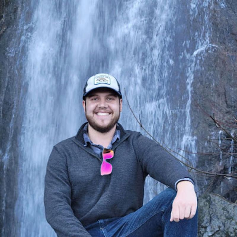 man kneeling in front of waterfall.