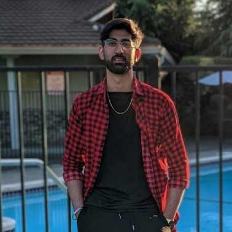 Man wearing black pants and shirt with a red checkered overshirt.