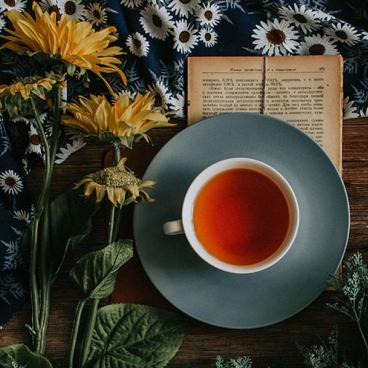 Cup of tea, flowers and a open book are on a table.