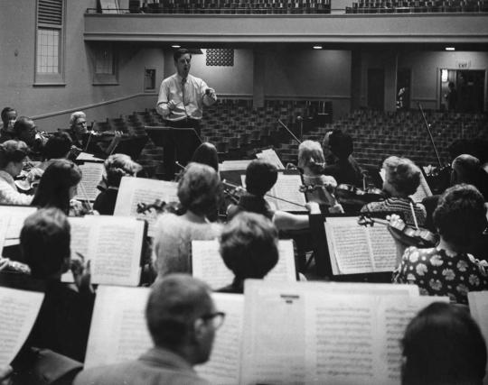 Person holding a baton directing musicians.