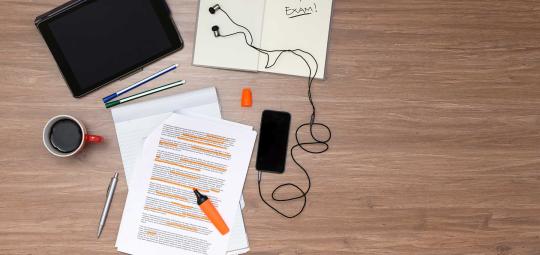 Pen, paper, phone, earbuds, tablet all on a table.