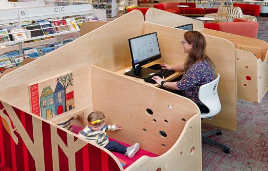 Parent working at a desk with an attached enclosed play area where her child is playing