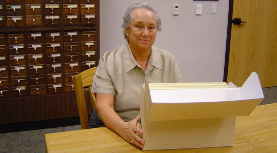 Woman sitting in front of a large box of paper.