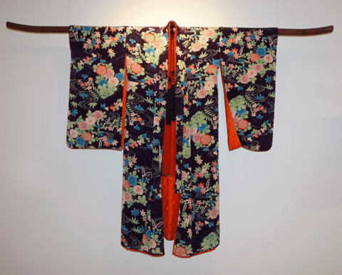 Kimono displayed on a wall. Black background with flowers of green, pink and blue. The inside of the kimono is red.