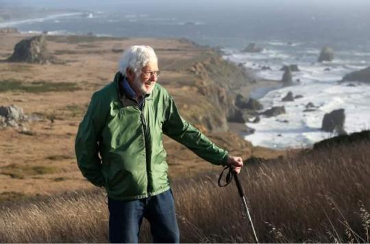 A man in a green jacket hiking along the California coast.