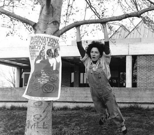 Woman in overalls swinging from a tree.